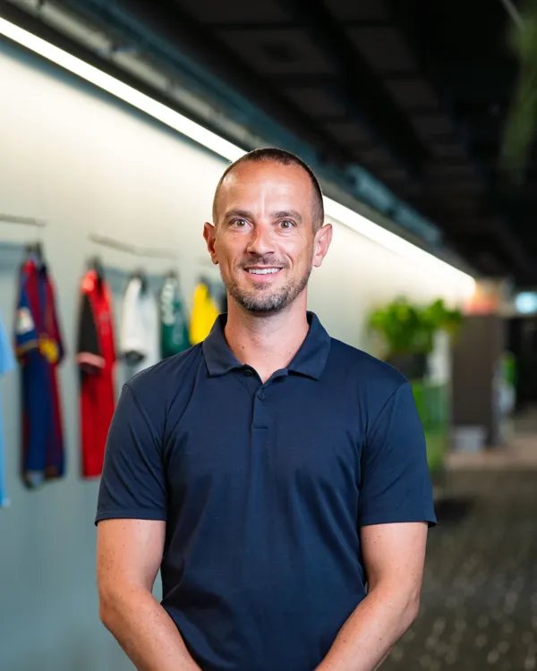 Mark Sampson in a navy polo shirt, in front of a wall of football shirts