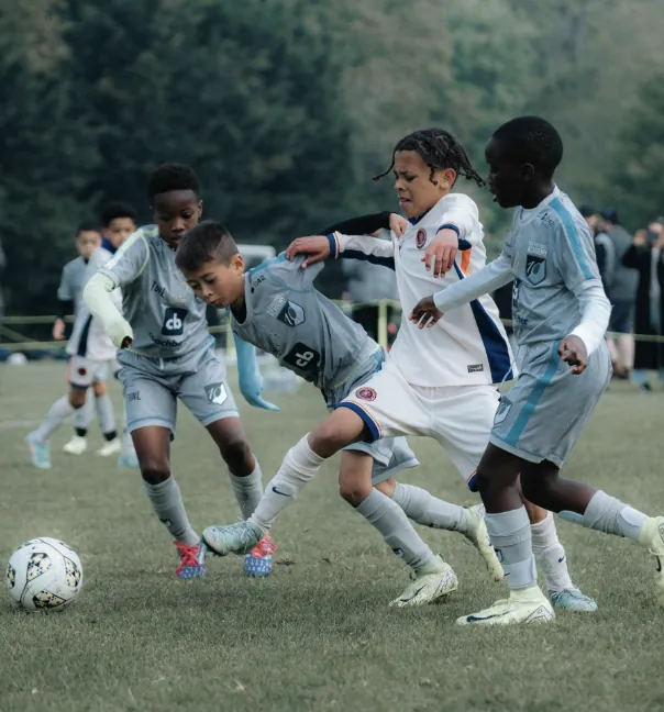 Elle Academy players in grey challenging a Chelsea FC youth player in white for the ball