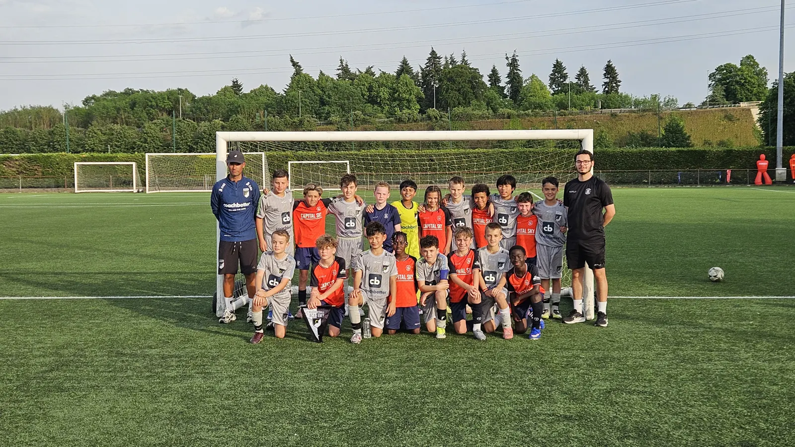 Elle Academy players in grey and a side in orange with their coaches in a joint team photo on a 3G pitch