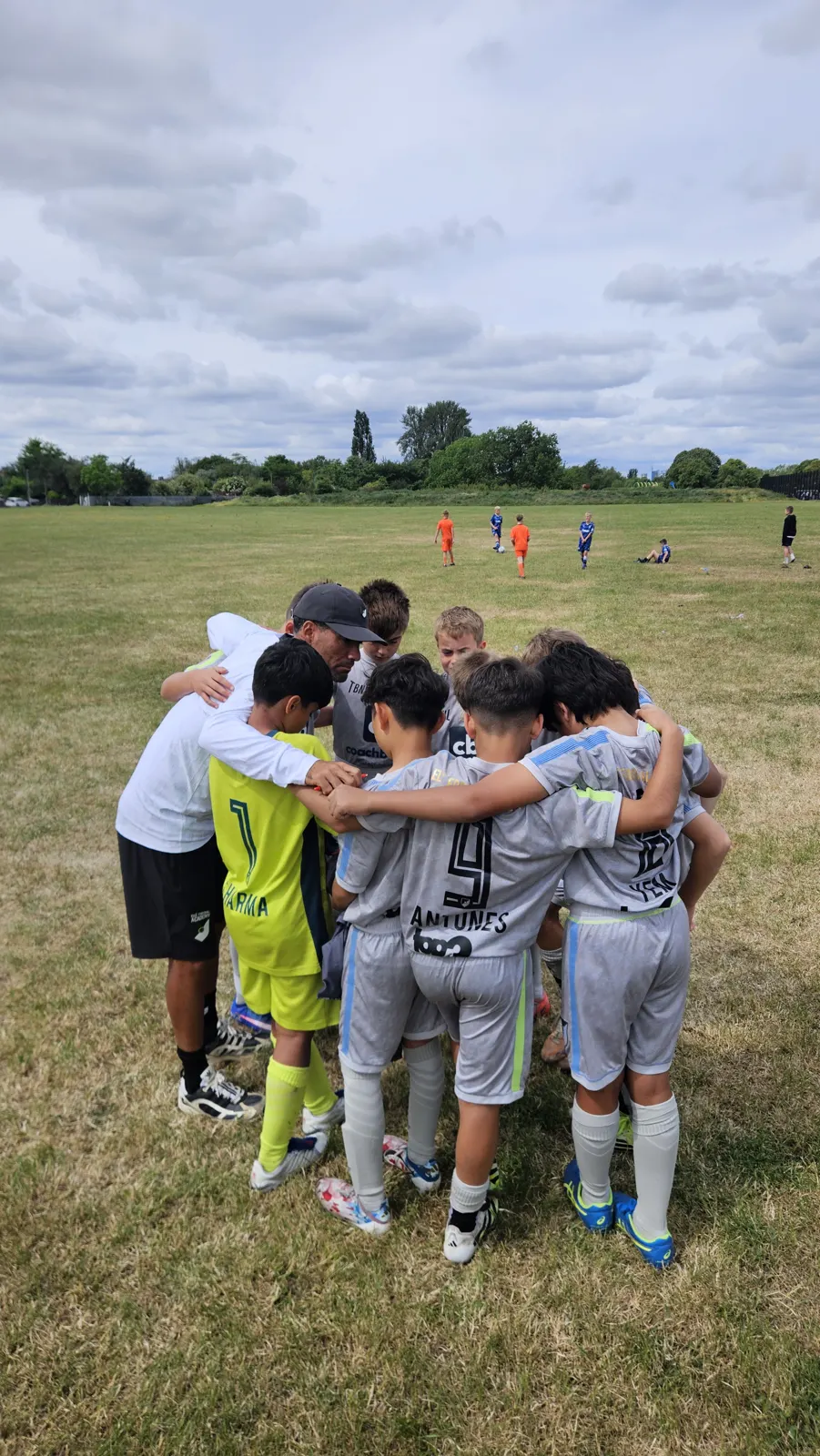 Elle Academy players in grey kits in a huddle with their coach on a grass pitch