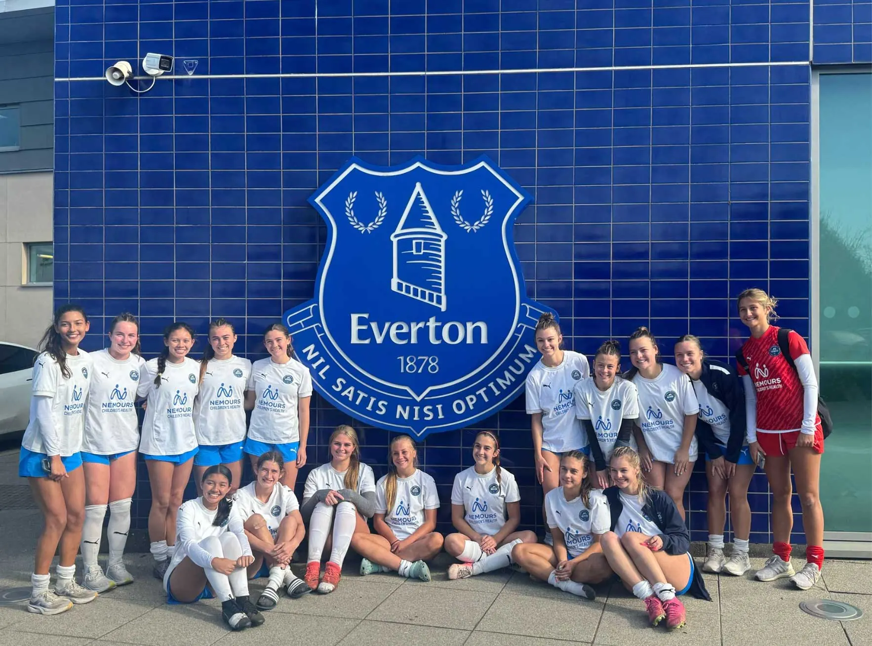 Jacksonville FC squad seated and standing in front of the Everton FC crest at Everton’s training facility