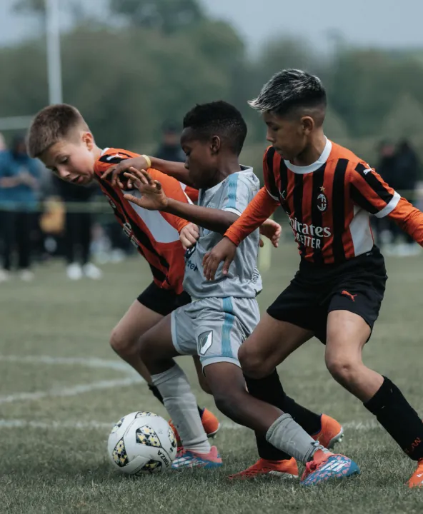 Elle Academy player in grey shielding the ball between two AC Milan youth players