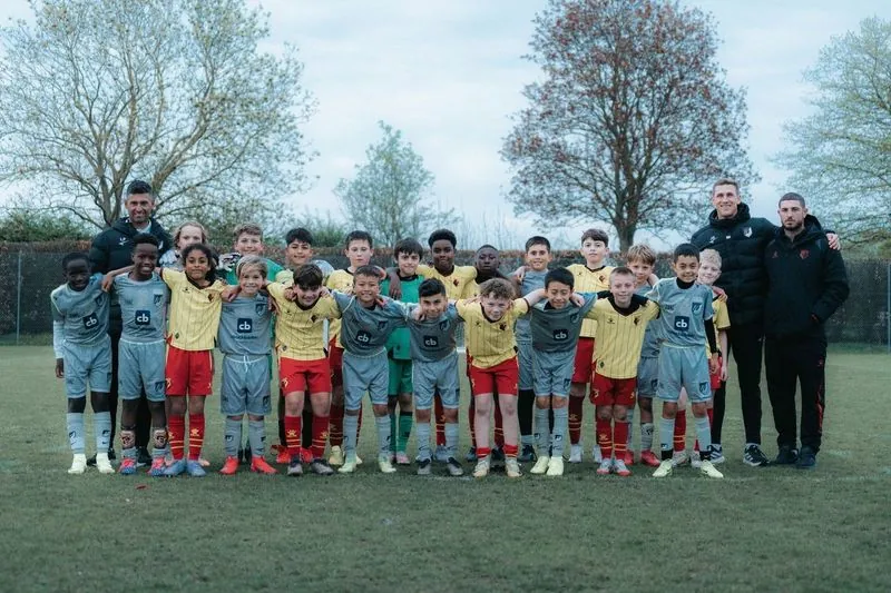 Elle Academy players in grey and Watford youth players in yellow and red, with four coaches, in a joint team photo on grass