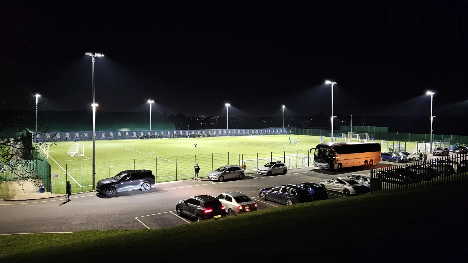 Birmingham City FC’s academy training ground under floodlights at night, with the team coach parked beside the pitches